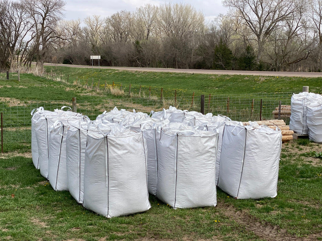 Large white bags on a grassy field with trees and a road in the background Cedar Barons Show Fiber 